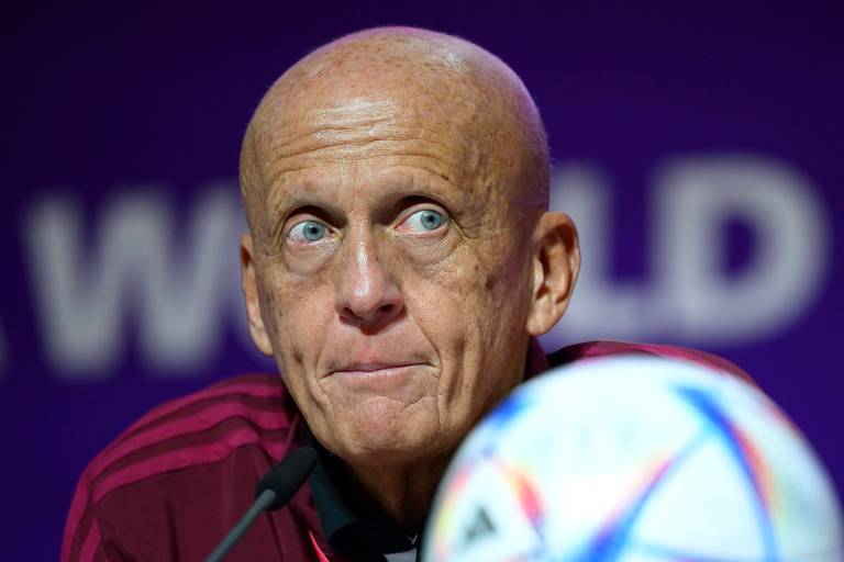 Close do rosto do ex-árbitro italiano Pierluigi Collina, chefe do comitê de arbitragem da Fifa, durante entrevista em Doha, no Qatar. Ele é careca, tem olhos claros e está olhando para o lado, À frente dele estão o microfone e uma bola de futebol 