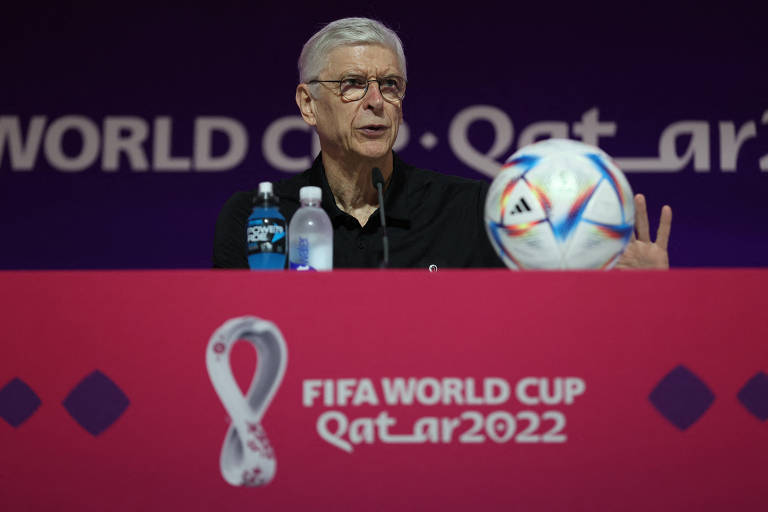 Arsène Wenger, chefe de desenvolvimento global de futebol da Fifa, durante entrevista em Doha, no Qatar; ele está sentado atrás de uma mesa e tem diante dele o microfone, duas garrafas de água e uma bola de futebol