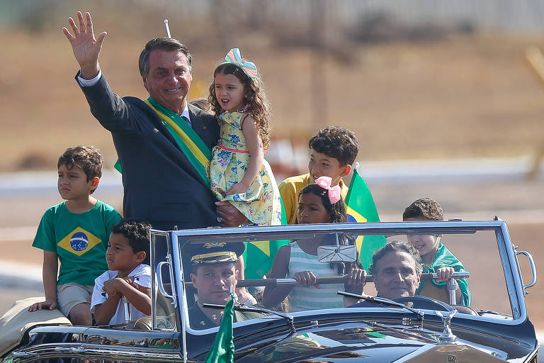 O presidente Jair Bolsonaro chega em carro aberto, dirigido pelo piloto Nelson Piquet, para a cerimônia de hasteamento da bandeira no Palácio da Alvorada