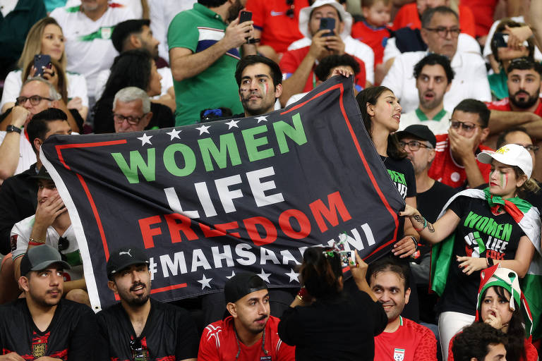 Torcedores com bandeira na aquibancada escrita "Women Life Freedom"