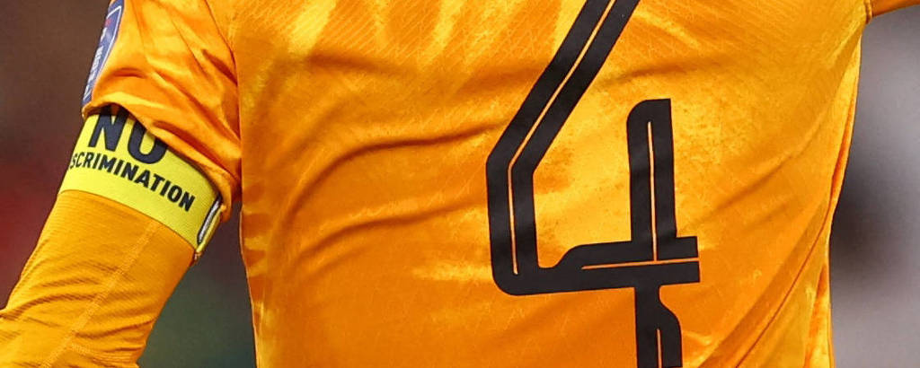Com uniforme laranja com o número 4 nas costas e apontando o dedo indicador da mão direita para o alto, Virgil van Dijk, capitão da Holanda na Copa do Qatar, usa tarja amarela no braço esquerdo com a inscrição 
