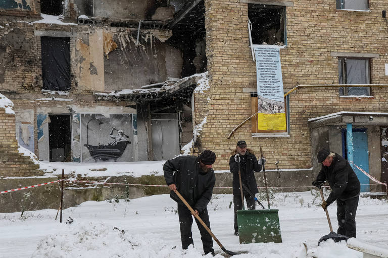 Ucranianos retiram neve em frente a prédio destruído em Horenka, nos arredores de Kiev