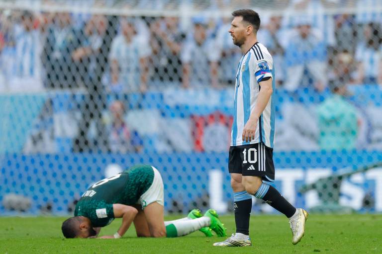 Messi anda com expressão desolada enquanto jogador da Arábia Saudita se ajoelha e encosta a cabeça no gramado