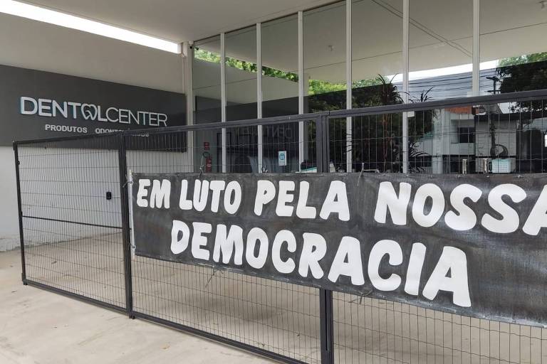 faixa preta escrito Luto pela nossa democracia em letras brancas em fachada de loja