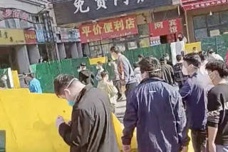 A group of people cross a downed fence following a protest at Foxconn's plant in Zhengzhou