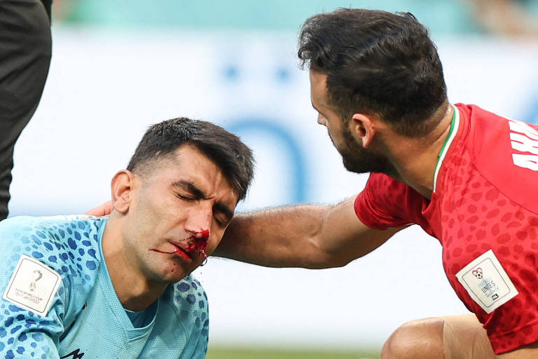 O goleiro Beiranvand, do Irã, sangra pelo nariz no jogo contra a Inglaterra depois de choque com companheiro de time na Copa no Qatar; ao seu lado, jogador iraniano ampara a cabeça dele