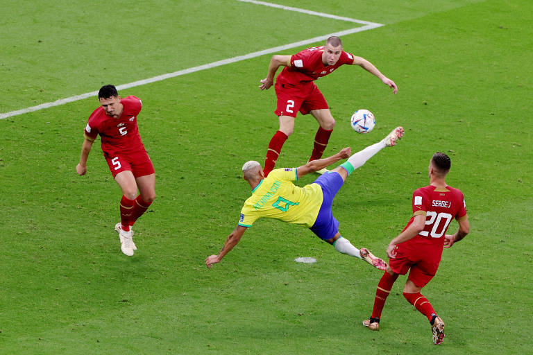 Richarlison, de uniforme camiseta amarela e shorts azul, está dando uma bicicleta, com a bola quase no pé, enquanto três jogadores da Sérvia, de vermelho, estão próximos, em movimento