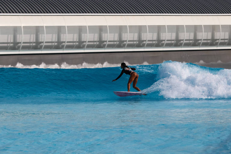 mulher em cima da sua prancha de surfe deslizando uma onda artificial