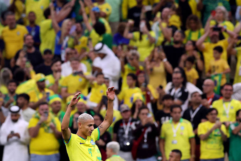 Richarlison ergue os braços em frente a arquibancada cheia de torcedores com camisetas do Brasil