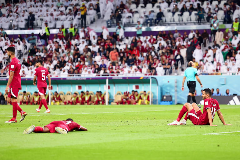 Um jogador do Qatar deitado e outro sentado no gramado, desconsolados após a derrota para Senegal no estádio Al Thumama, em Doha