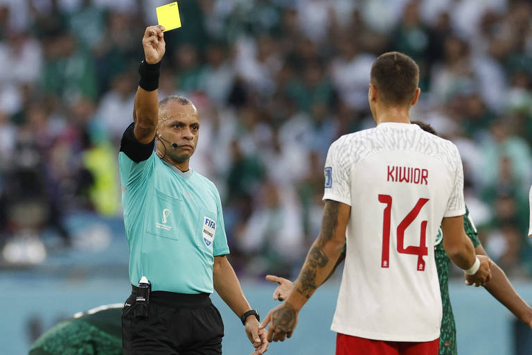 O árbitro brasileiro Wilton Sampaio mostra cartão amarelo para Jakub Kiwior, que usa camisa com o número 14, em Polônia x Arábia Saudita no estádio Cidade da Educação, em Al Rayyan, no Qatar