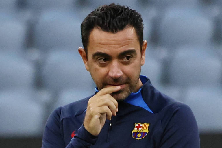 Imagem colorida mostra o técnico Xavi, do Barcelona, da cintura para cima. Ele está de frente, com os braços cruzados e o dedo indicador da mão direita encostado nos lábios.