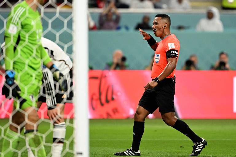 Com camisa laranja e calção e meias pretas, o árbitro de El Salvador Iván Barton dirige a palavra a jogadores alemães na partida entre Alemanha e Japão na Copa do Mundo do Qatar, em Doha