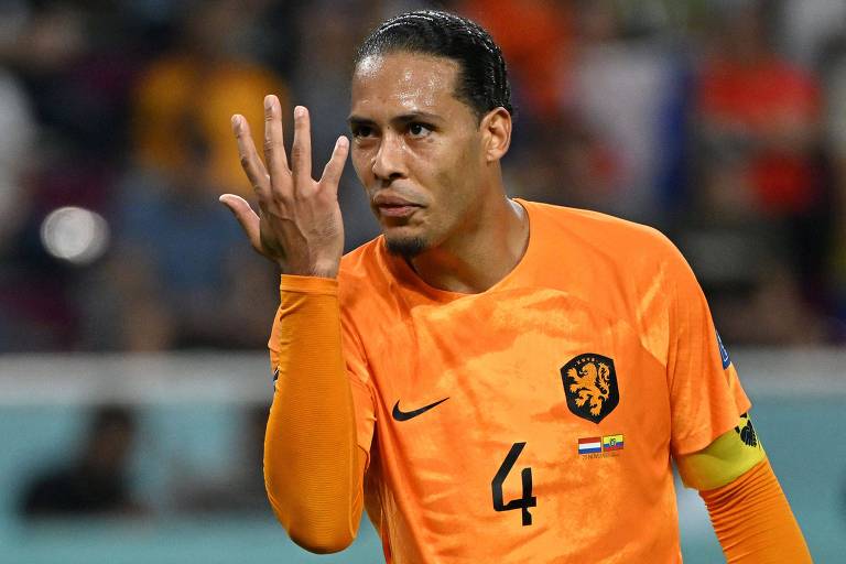 Virgil van Dijk, capitão da Holanda, com a palma da mão aberta diante do rosto no jogo contra o Equador na Copa do Mundo do Qatar; seu uniforme é laranja, com o número 4 em preto no centro da camisa, e ele usa uma braçadeira amarela, de capitão, no braço esquerdo