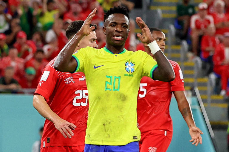 Vinicius Junior, usando a camisa da seleção brasileira com o número 20 e na cor amarela, ergue os braços e expressa no rosto um tom de lamento na partida em que o Brasil derrotou a Suíça por 1 a 0 no estádio 974, em Doha, no Qatar, na Copa do Mundo