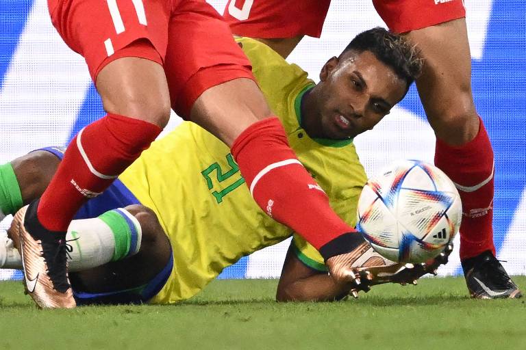 Imagem colorida mostra Rodrygo caído no chão, com a cabeça virada para a direita, entre as pernas de dois jogadores da Suíça.