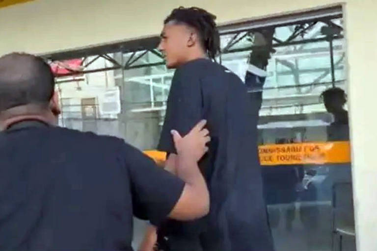 Imagem mostra homem negro de dreads sendo levado por um policial negro para dentro da delegacia
