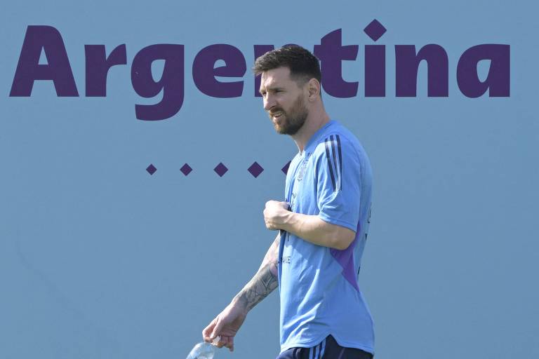 Com camiseta azul clara, o atacante Messi caminha em treino na Universidade do Qatar, em Doha; atrás dele, em um painel, está escrita a palavra "Argentina"