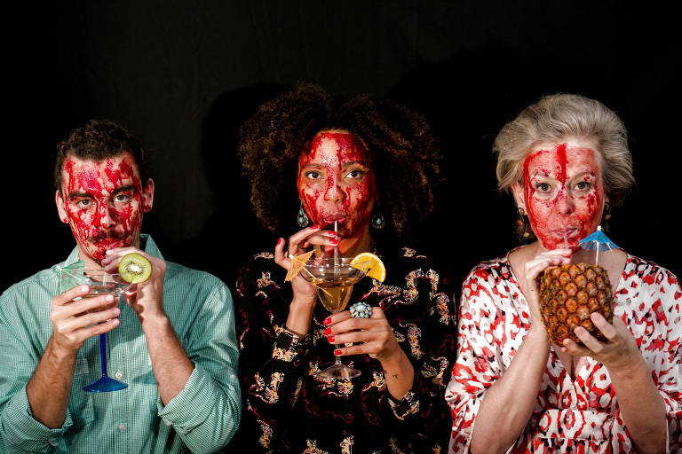 Três personagens, um homem e duas mulheres, tomam um drinque com o rosto sujo de sangue