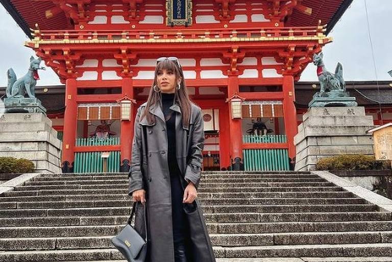 Em foto colorida, mulher posa em frente a um templo japonês