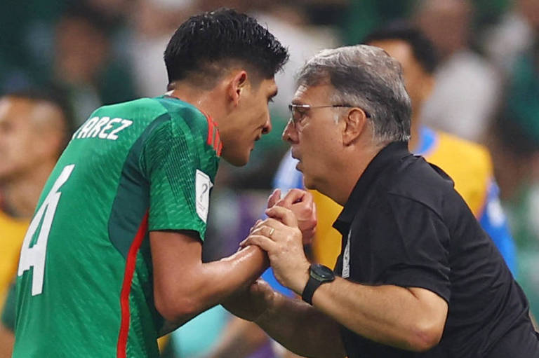 Imagem colorida mostra, do tronco para cima, o técnico Gerardo Martino, à esquerda, virado para a direita, segurando as duas mãos do jogador mexicano Alvarez, enquanto fala bem perto do rosto dele.