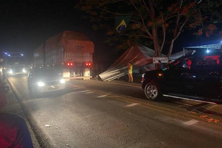 A imagem mostra caminhões e carros e uma tenda caída à beira de uma estrada