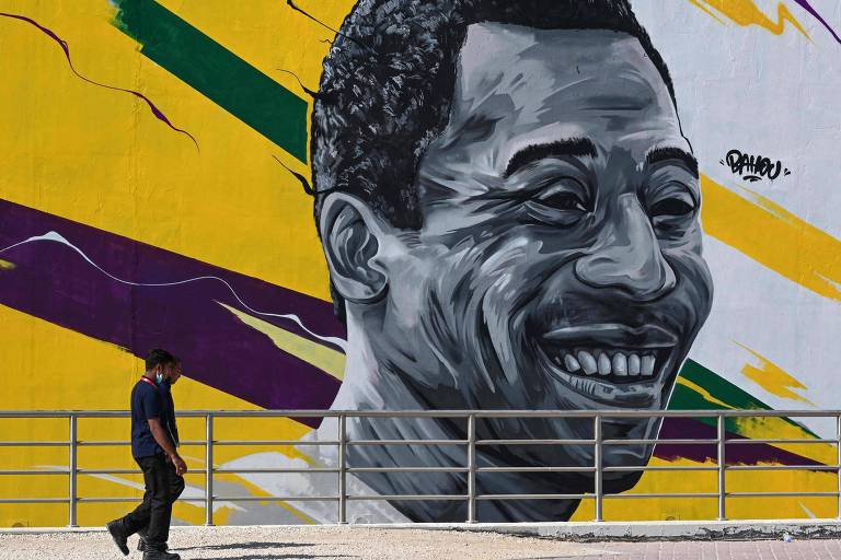 homem caminha diante de mural pintado com o rsoto de homem negro e cores amarela, verde e roxa ao fundo