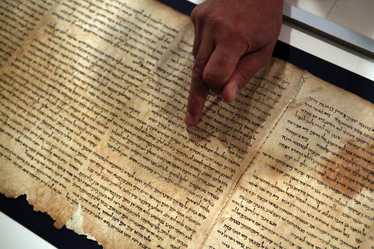 Homem com mão morena mostra pergaminho amarelado em hebraico com texto do livro do profeta Isaías 