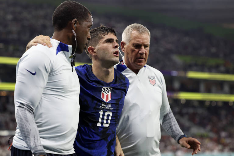 Pulisic, o craque da seleção dos EUA, deixa o campo amparado por dois membros do estafe norte-americano depois de se lesionar no gol que fez contra o Irã, em Doha, no jogo final da fase de grupos da Copa do Mundo