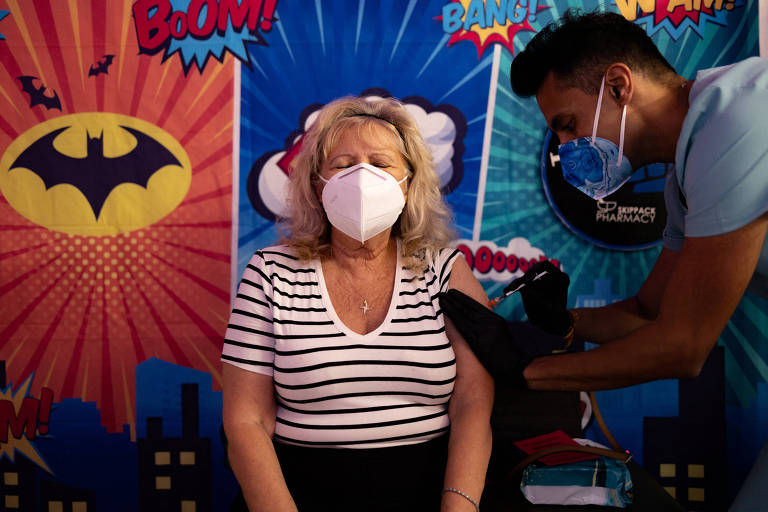 idosa recebe vacina contra covid no braço. usa máscara, está sentada