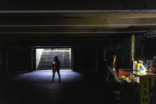 A woman carrying a flashlight passes by a lantern-lit shop in an underground passage in a neighborhood in Kyiv, Ukraine that has experienced persistent power outages after Russian attacks on Ukrainian infrastructure, on November 29, 2022. (David Guttenfelder/The New York Times)