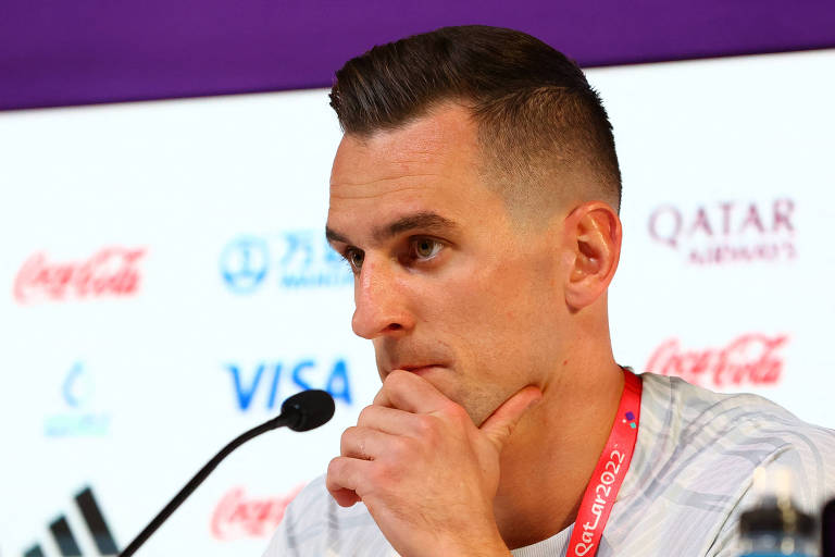 Com a mão esquerda no queixo e o microfone diante dele, o atacante polonês Milik ouve pergunta durante entrevista no Centro de Imprensa de Doha na véspera do duelo com a França na Copa do Qatar