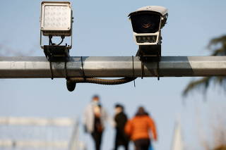 Pedestrians walk on an overpass near a surveillance camera overlooking a street in Beijing