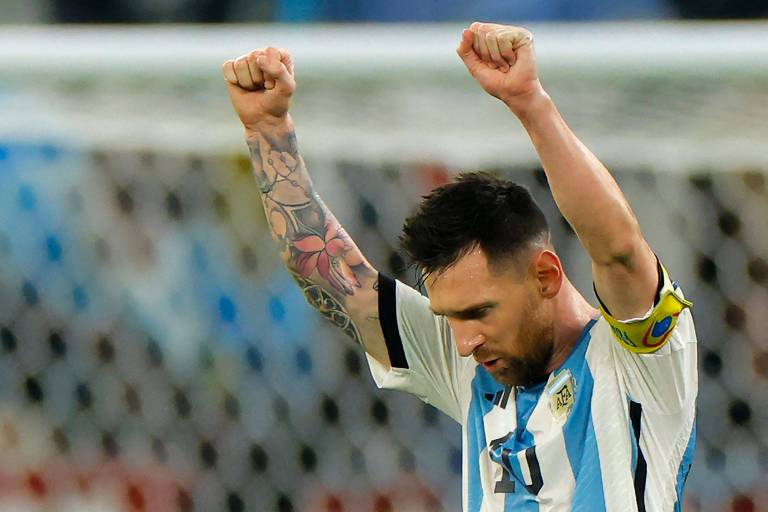 Imagem colorida mostra Messi, do tórax para cima, voltado para a esquerda, com a cabeça levemente abaixada e com os dois braços levantados e punhos cerrados.