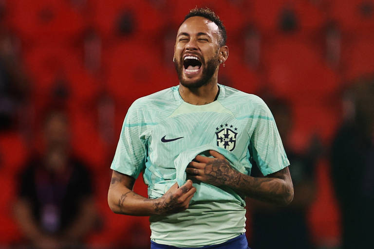 Neymar sorri e segura a camisa de treino, verde-clara, na altura do peito