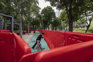 A lone woman sneaks into an exercise area at a park that had been cordoned off by red plastic barriers, near Xiasha Village in Shenzhen, China on Nov. 16, 2022. (The New York Times)