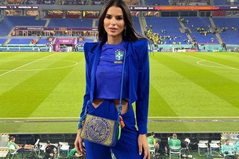 Em foto colorida, mulher de azul posa em estádio
