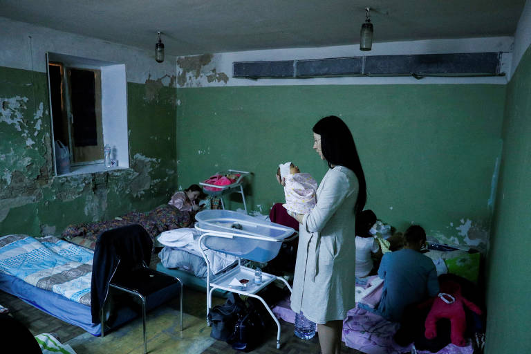Mulheres com filho recém-nascido se abriga com outras pessoas em porão de maternidade durante ataque russo em Kiev, na Ucrânia
