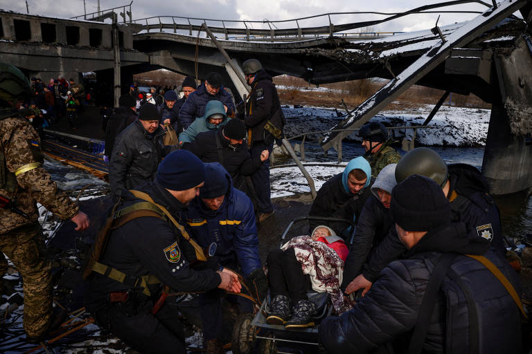 Homens carregam mulher enquanto fogem do avanço das tropas russas em Irpin, nos arredores de Kiev, na Ucrânia