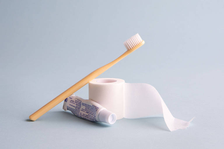 Escova de dente apoiada em pasta de dente e rolo de fita