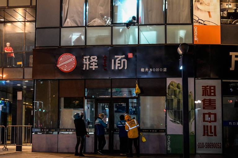 Funcionário de restaurante fechado pelas restrições da pandemia entrega comida pela janela para entregador em Pequim 
