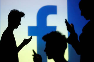 FILE PHOTO: People pose with mobile devices in front of projection of Facebook logo in this picture illustration taken in Zenica