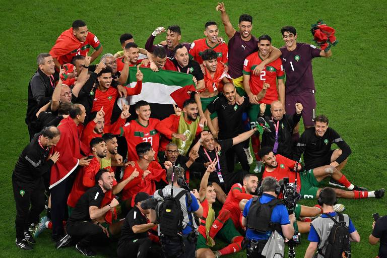 Jogadores e comissão técnica de Marrocos comemoram a classificação em campo, com a bandeira da Palestina no centro