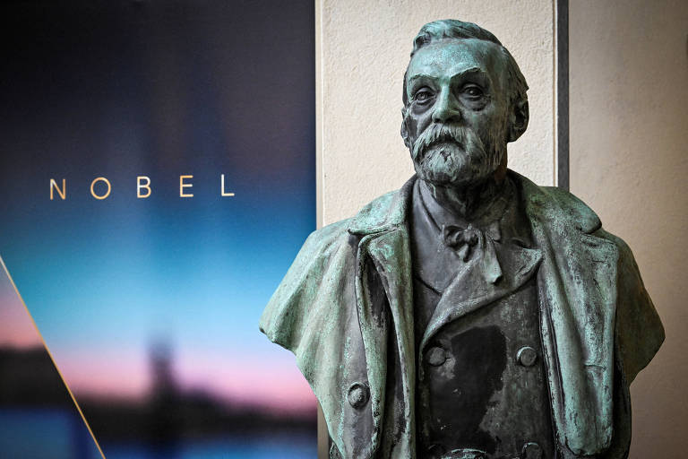 Estátua de mármore representa homem de barba e bigode; ao fundo, está escrito Nobel