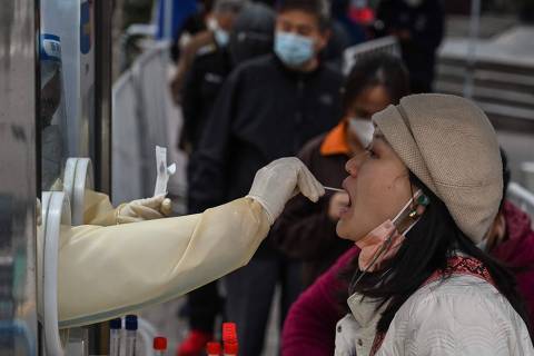 A health worker takes a swab sample from a woman to test for the Covid-19 coronavirus in the Jing'an district in Shanghai on December 7, 2022. (Photo by Hector RETAMAL / AFP)