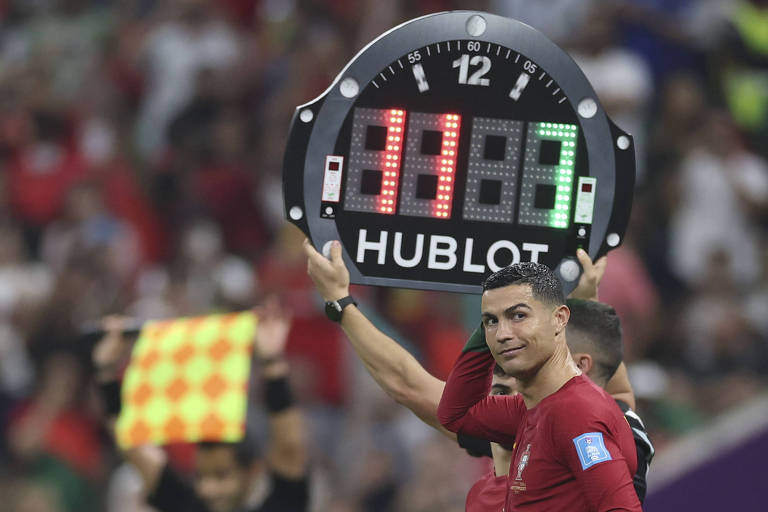 Imagem colorida mostra Cristiano Ronaldo olhando para o lado, enquanto uma placa com os números 11, em vermelho, e sete, em verde, e levantada sobre ele.