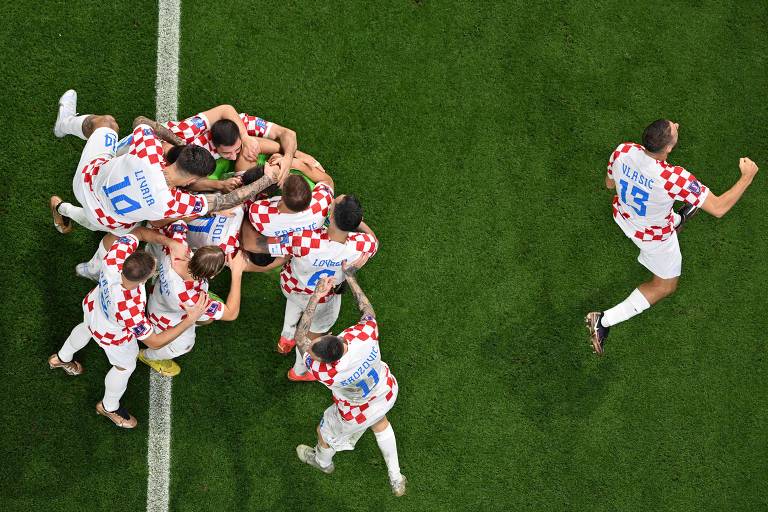 Imagem aérea de jogadores croatas se abraçando e vibrando em campo, usando uniforme com xadrez vermelho e branco