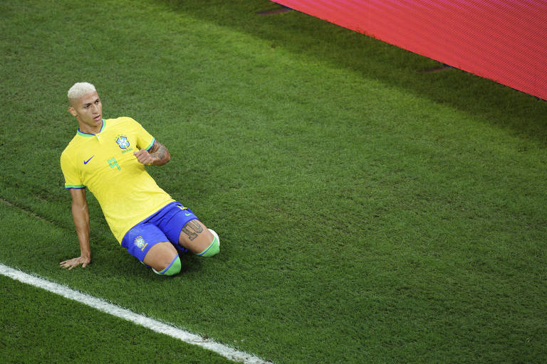 Com camisa amarela e calção azul, Richarlison desliza de joelhos no gramado do estádio 974 para festejar seu gol na goleada por 4 a 1 do Brasil sobre a Coreia do Sul nas oitavas de final da Copa do Qatar 
