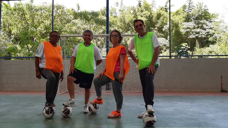quatro idosos de pé, com camisetas coloridas, em quadra de futebol