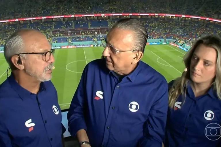 Em foto colorida, trio de comentaristas conversam em um estúdio no estádio de futebol